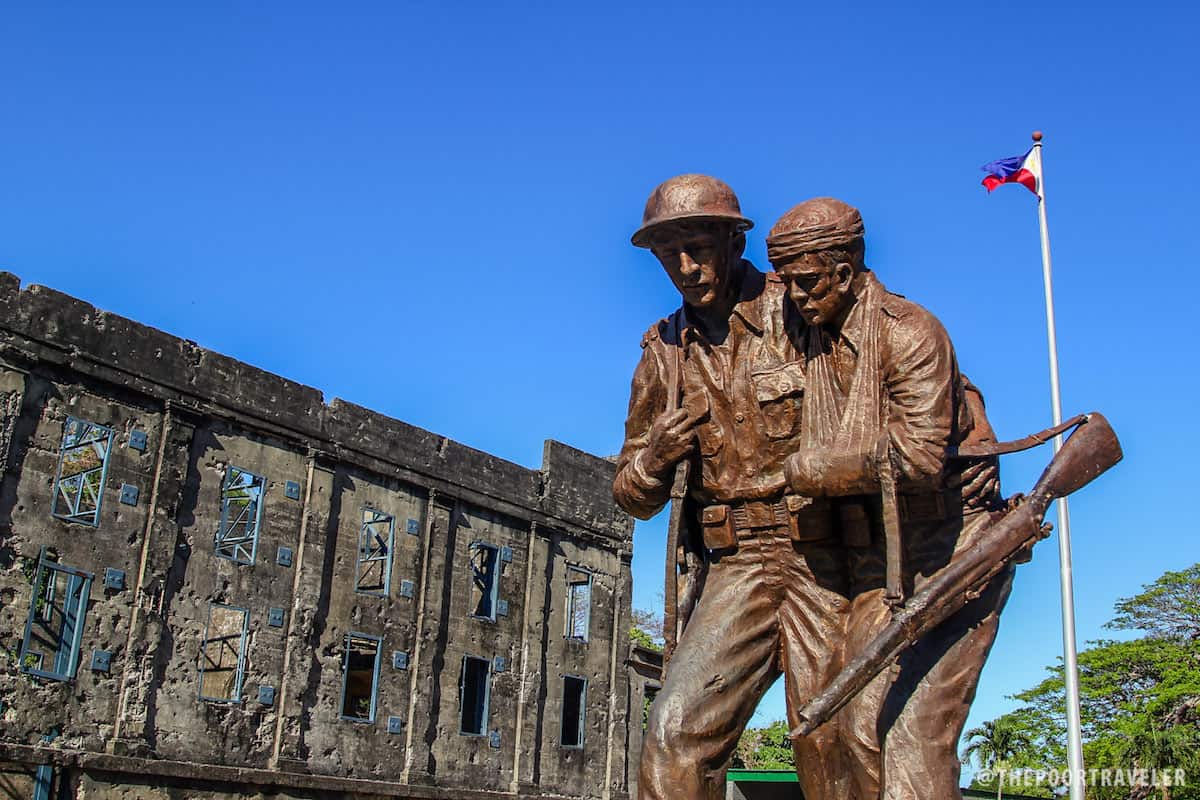 美国和菲律宾人的雕像在背景中带有Cine Corregidor和菲律宾国旗的废墟。